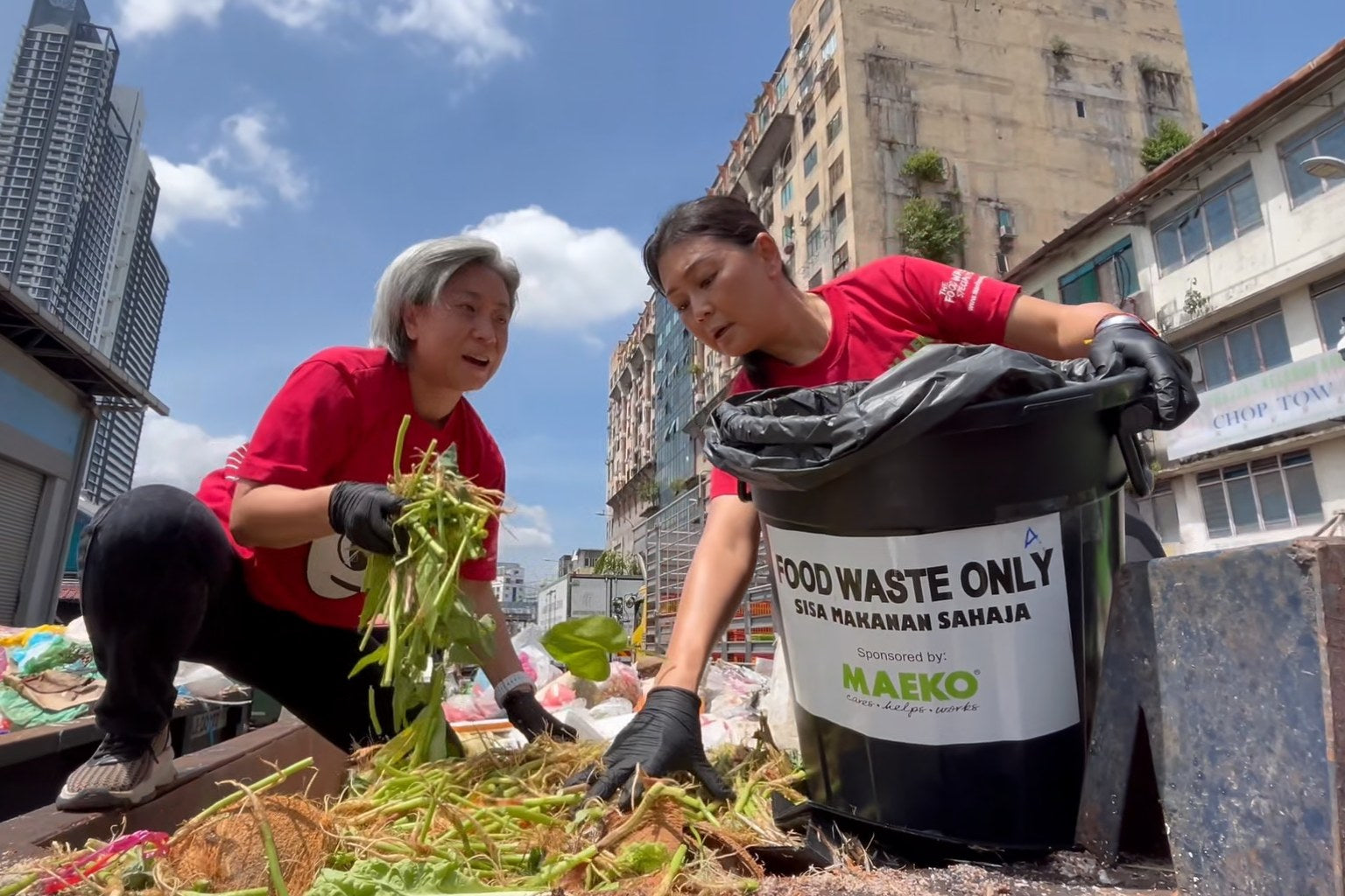 Two MAEKO team members in red shirts sorting market food waste into a MAEKO food-waste bin.