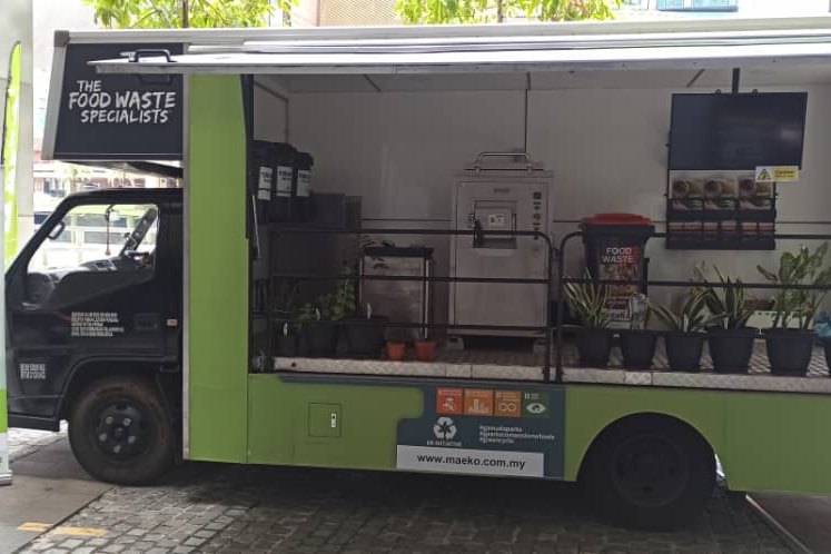 The Composting-on-Wheels truck with its side open, potted plants and a display inside, parked at a kerb.