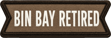 An embroidered patch in tan twill with a dark brown merrow edge, lettered BIN BAY RETIRED in bone satin-stitch condensed capitals on one line