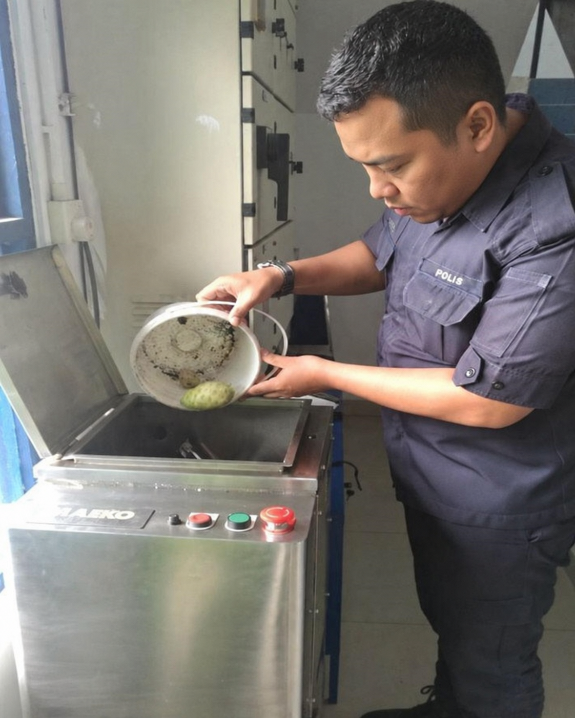 A police officer tips a stainless bowl of food scraps into the open lid of a MAEKO composter.