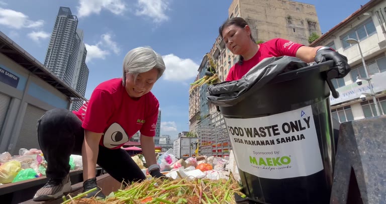 Two people in red MAEKO tees sorting food waste at a wet market